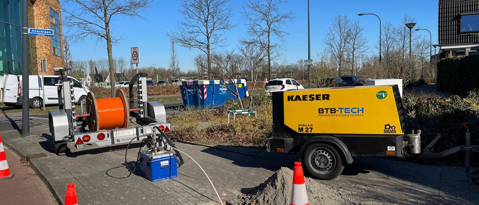 Afgezette werklocatie met haspelwagen en compressor in een woonstraat