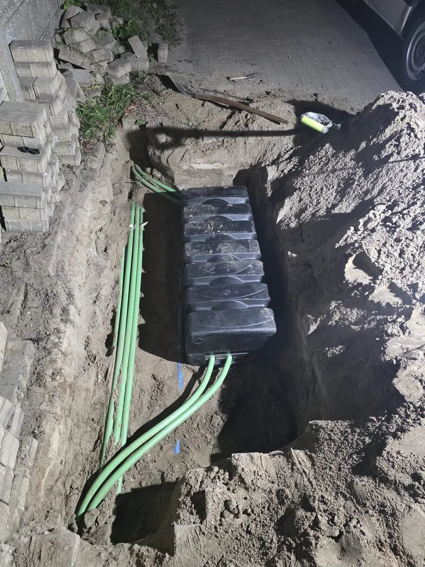 Nieuwe handhole en HDPE-buizen in de sleuf tijdens nachtelijk herstel van de ringverbinding