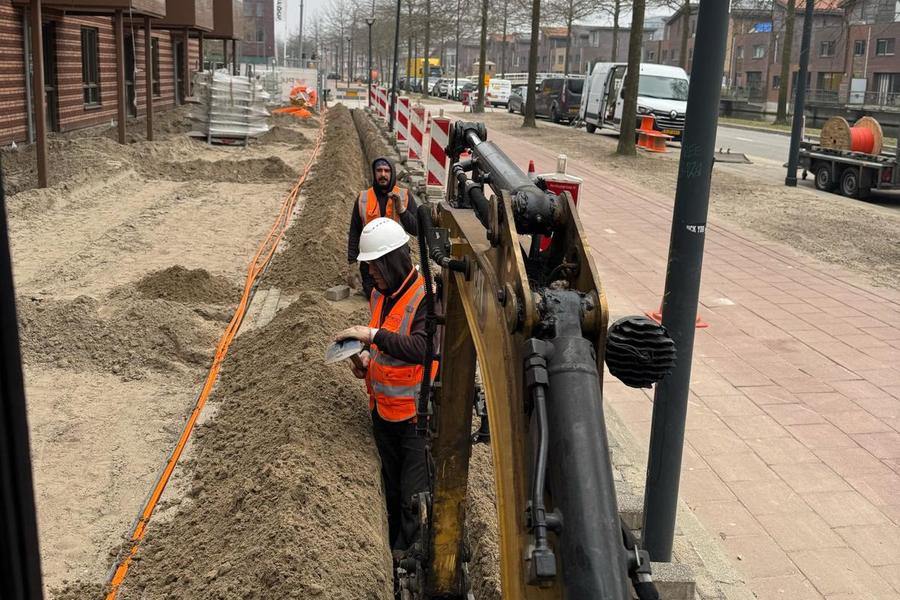 Monteurs leggen glasvezeltracé aan in een sleuf langs nieuwbouw